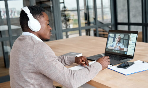Serious african business man or black male student wearing headphones conference video calling, watching webinar online, social distance learning or working using laptop at home office, taking notes.